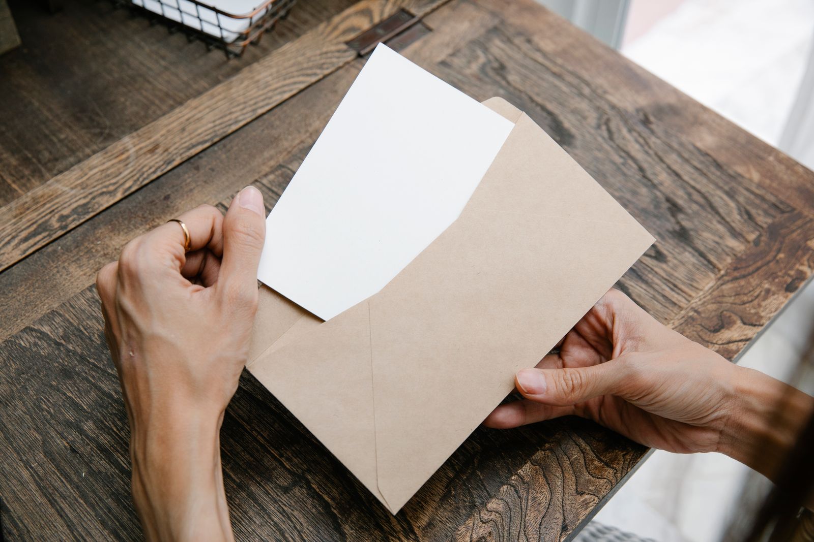 Hands taking a letter out of an envelope at a wooden table